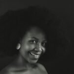 Monochrome close-up portrait of a smiling woman with afro hairstyle.